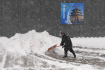 Muž odklízí sníh před hotelem v Pekingu, který 13. února 2022 zasáhlo husté sněžení.