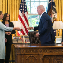Prezident Joe Biden předává jedno z per poslankyni Elisse Slotkinové, kterým podepsal zákon o půjčce a pronájmu na obranu demokracie na Ukrajině. Pondělí 9. května 2022 ve Washingtonu, za účasti viceprezidentky Kamaly Harrisové (vlevo) a senátora Bena Cardina (vpravo).